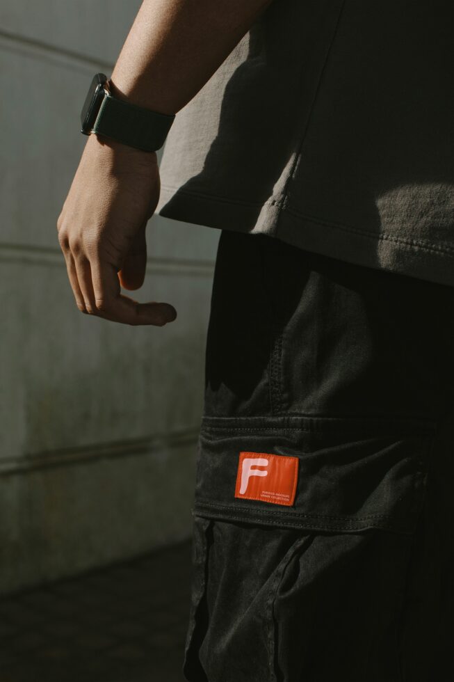 Person wearing black cargo pants with orange woven label patch, smartwatch, natural lighting