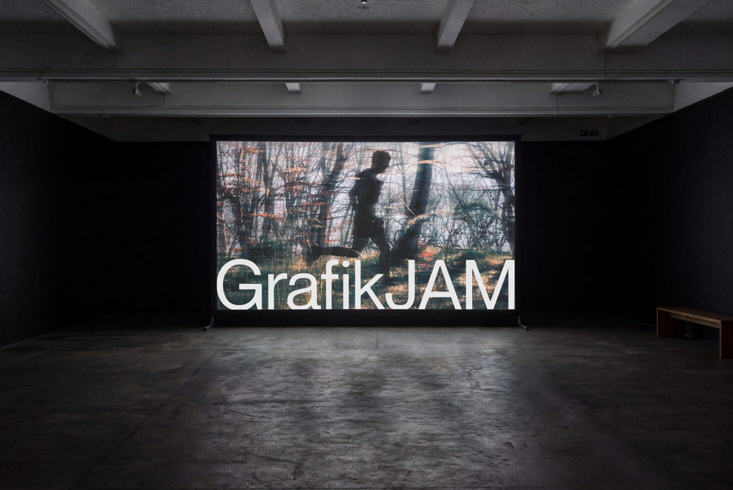 Large gallery screen displaying GrafıkJAM text overlay on forest imagery in minimal concrete space