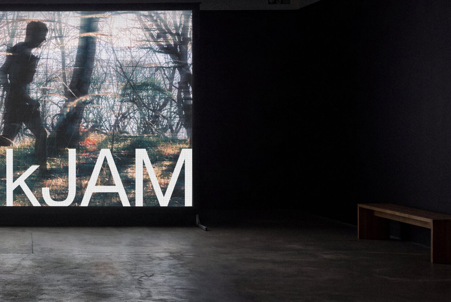 Large projection screen displaying bare trees with white "KUAM" text overlay in gallery space