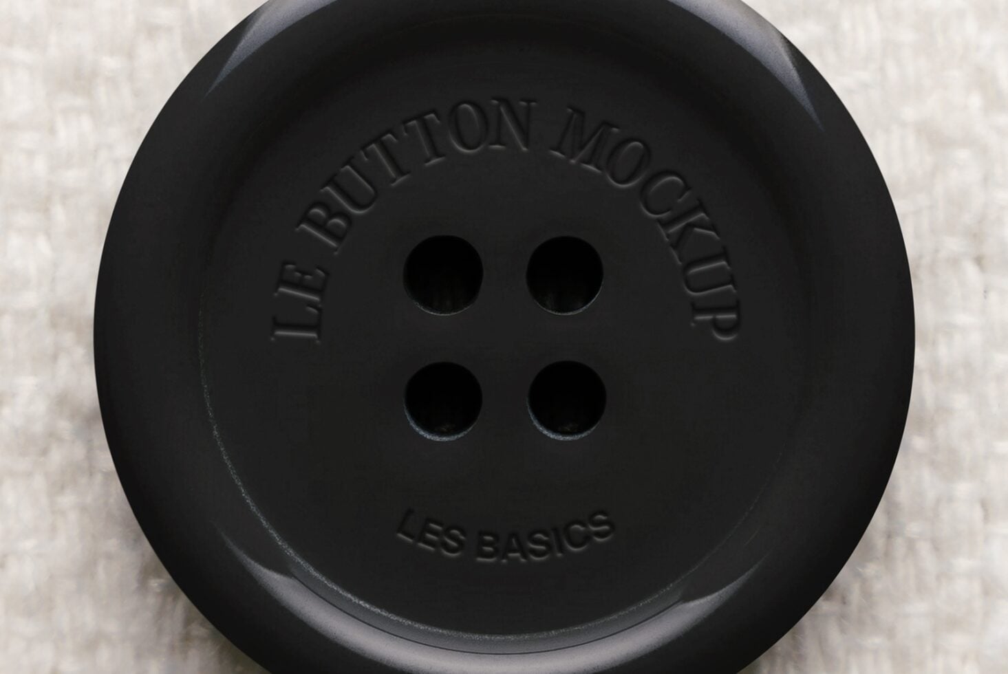 Oversized black button with embossed text, four holes, shot flat lay on cream texture
