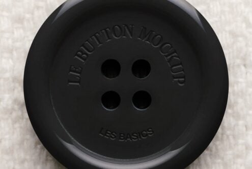 Oversized black button with embossed text, four holes, shot flat lay on cream texture