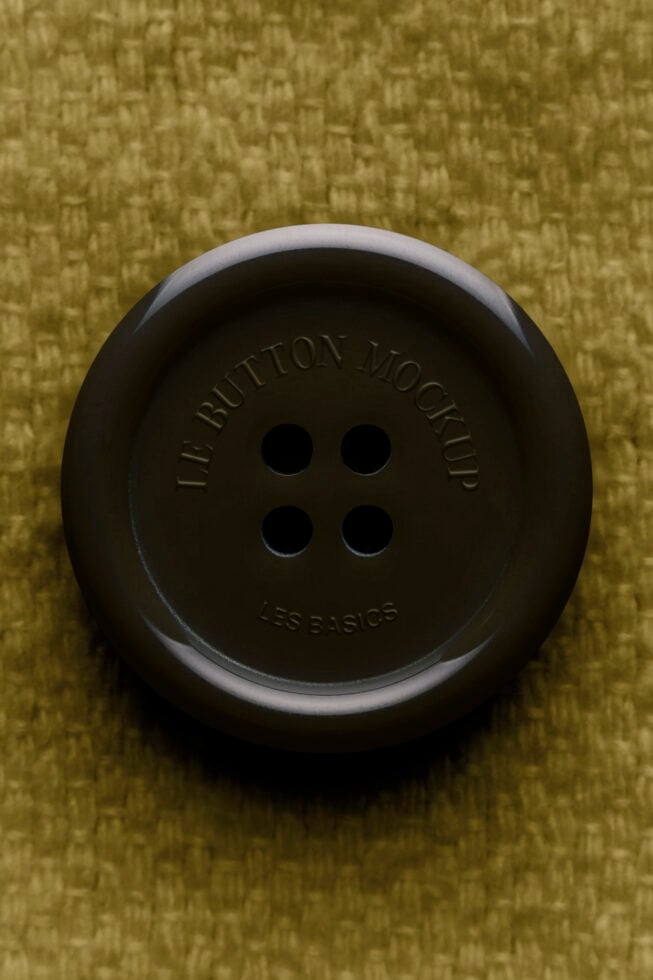 Overhead shot of black button with four holes on olive textured fabric background