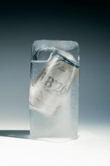 Frozen cash bundle wrapped in plastic with ice crystals on gray backdrop