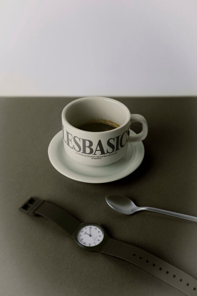 Coffee cup mockup with saucer, spoon, watch on neutral backdrop
