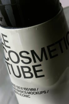 Cosmetic tube mockup shot at an angle showing white label with bold black typography