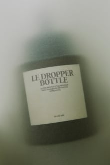 Minimalist dropper bottle mockup with cream label on soft green fabric backdrop