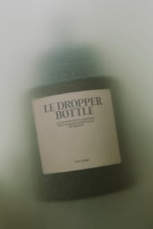 Soft-focus dropper bottle mockup with cream label on sage green background