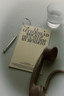 Cream letterhead mockup hanging with pen, vintage phone, textured glass on gray surface