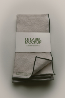 Folded linen napkin with white band label showing green text, corner peeled back to reveal texture