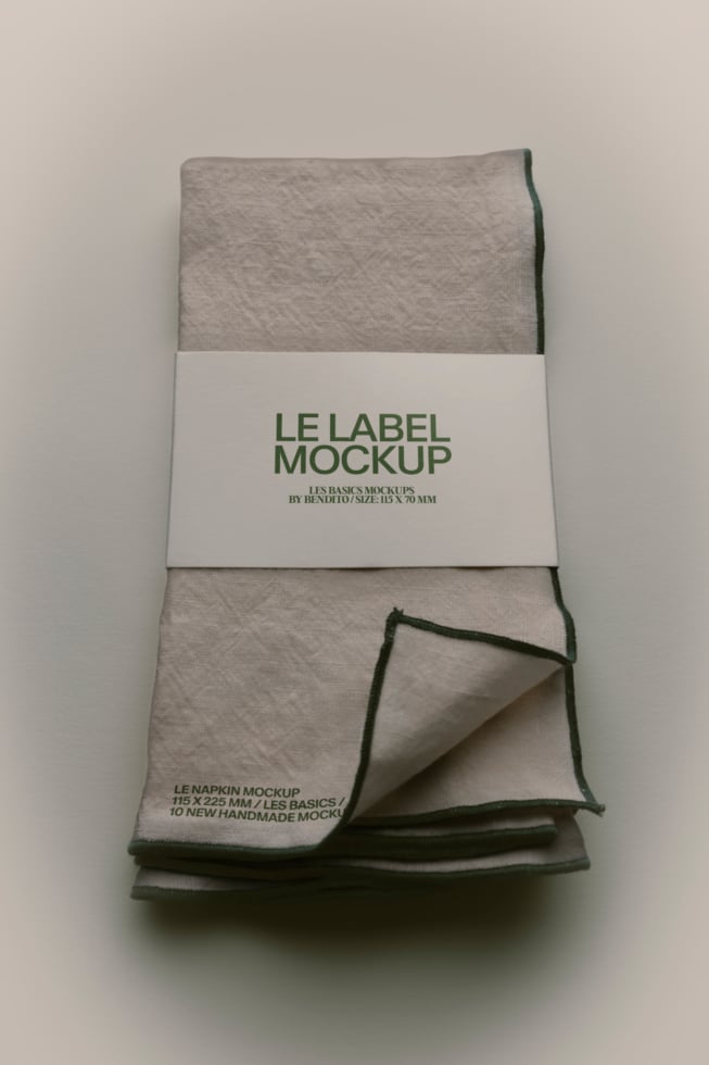 Folded linen napkin with white band label showing green text, corner peeled back to reveal texture