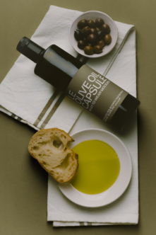 Olive oil bottle mockup styled flat lay with bread, olives, bowl of oil, linen napkin on sage background