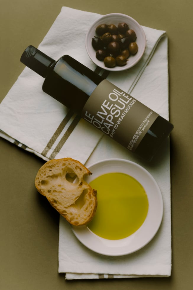 Olive oil bottle mockup styled flat lay with bread, olives, bowl of oil, linen napkin on sage background