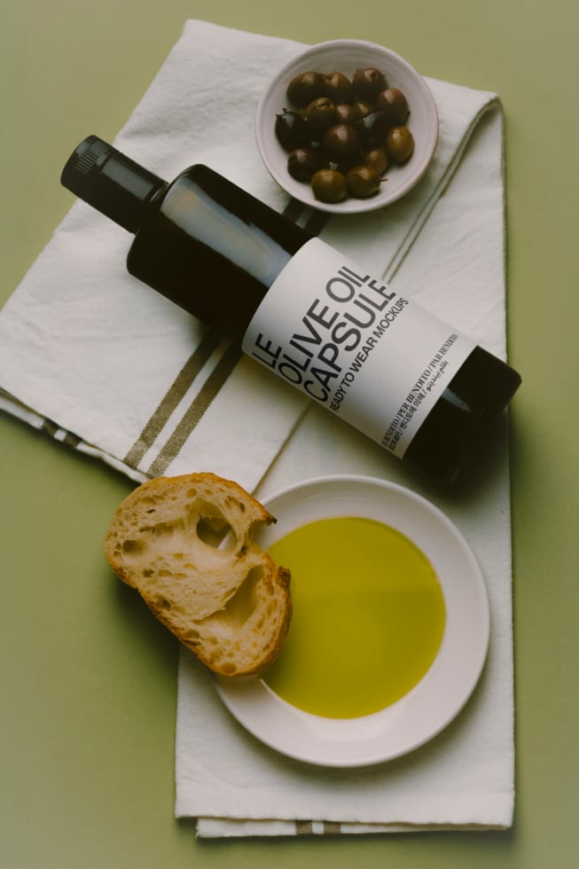 Olive oil bottle mockup with bread, olives, oil in bowls on linen cloth