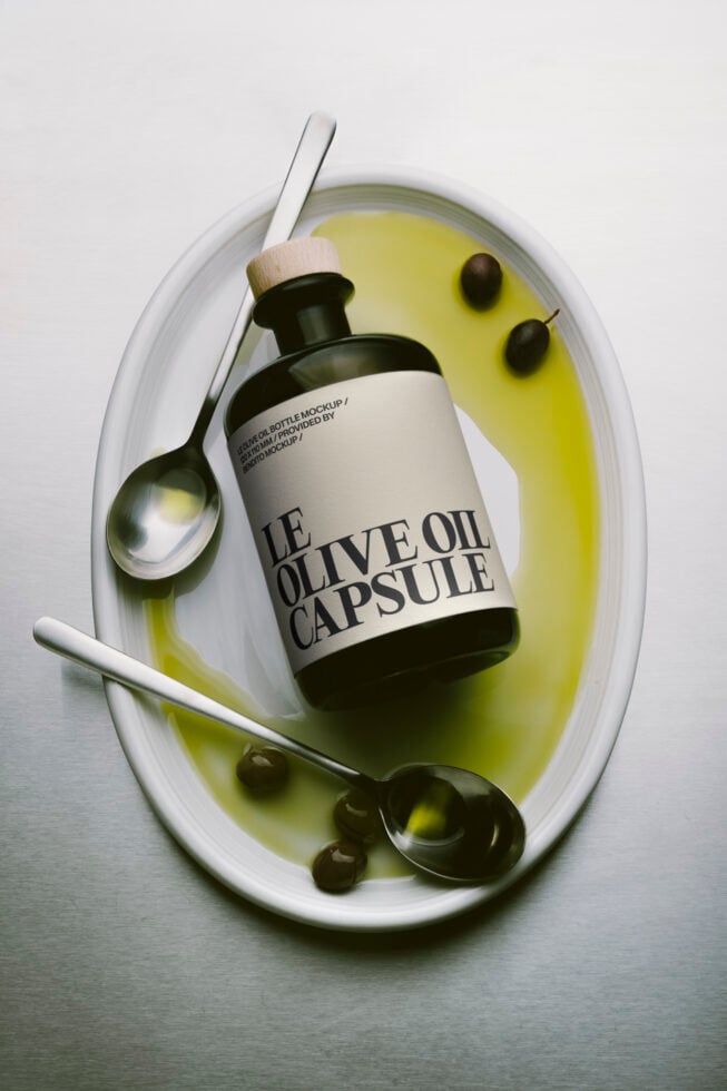 Olive oil bottle mockup styled on white plate with olives, spoon, brush overhead shot