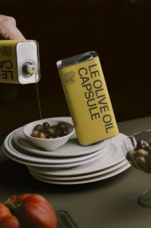 Olive oil can pouring into bowl with olives, stacked plates, dark moody setup