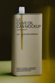 Tall rectangular olive oil can with white cap, cream label showing golden oil drip, dark text layout on soft yellow green background