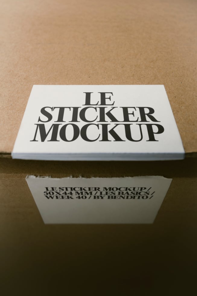 Square white sticker on kraft paper with serif typography, shot from above with natural shadow