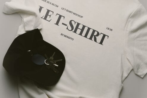 Cream tee lying flat with serif text design, black hat with keys beside it