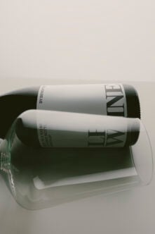 Two dark glass bottles with white labels stacked in clear cylinder packaging against neutral background