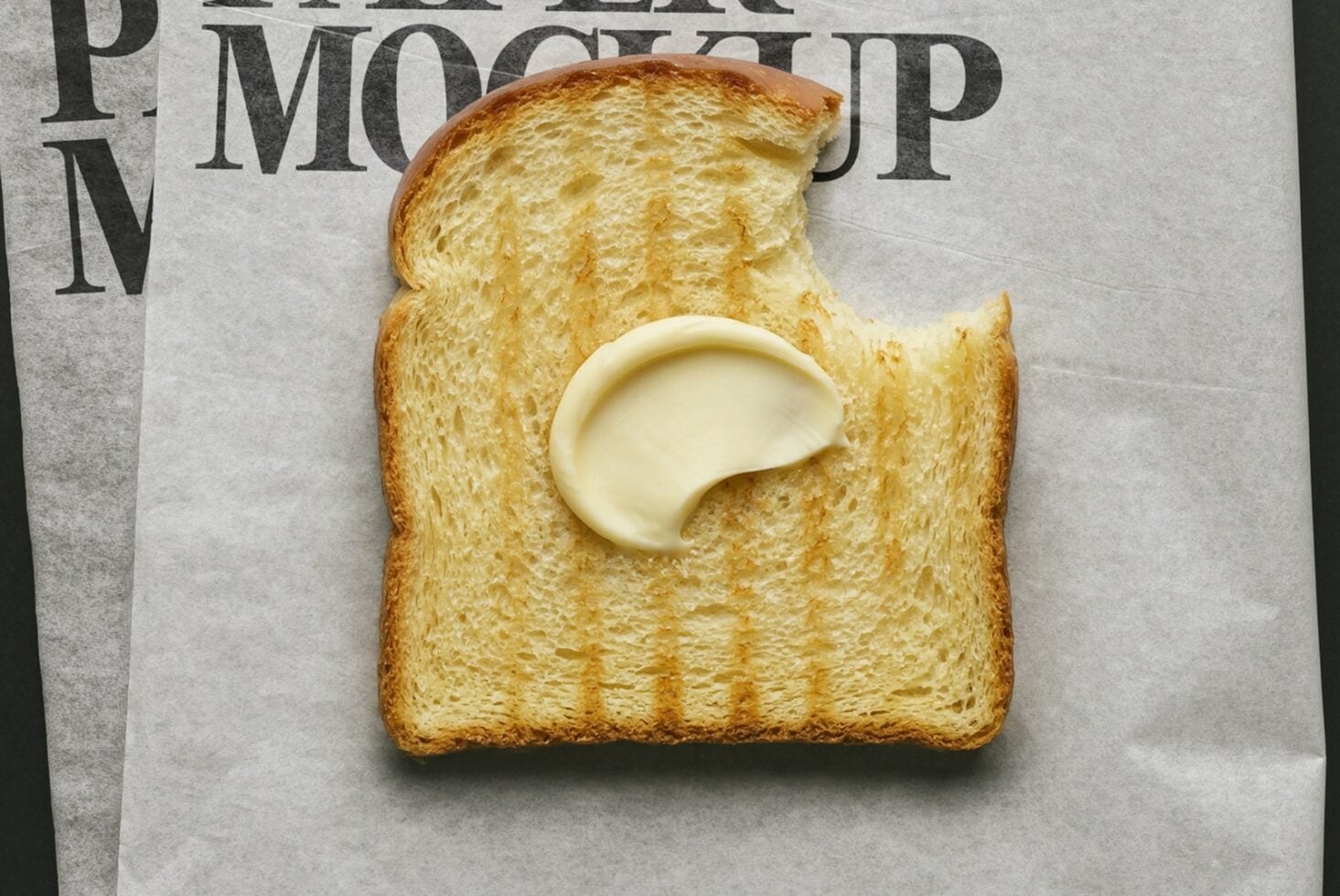 Buttered toast with bite taken out on newspaper, melting butter pat in center