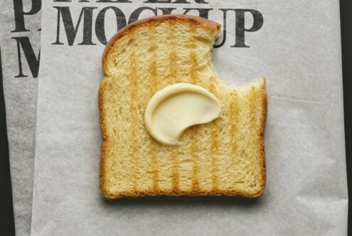 Buttered toast with bite taken out on newspaper, melting butter pat in center