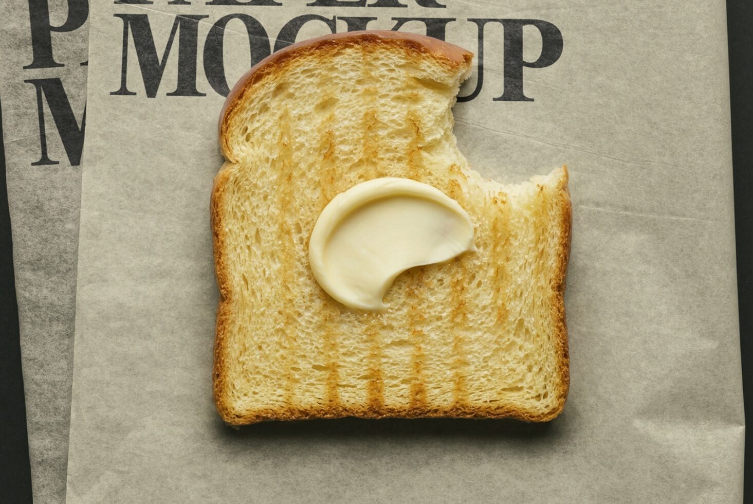 Buttered toast with bite taken out, sitting on newspaper with serif typography