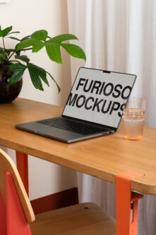 Laptop mockup on wooden desk with plant, water glass, orange chair in natural light