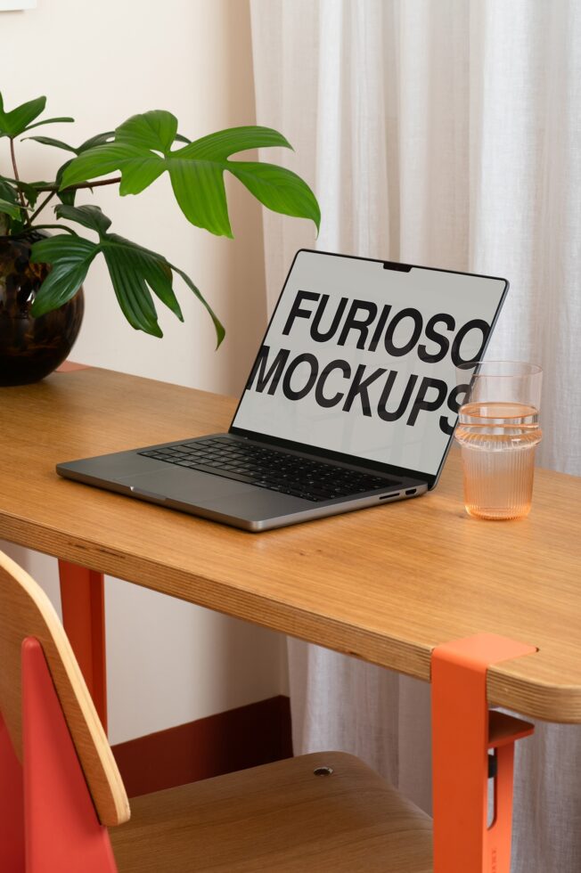 Laptop mockup on wooden desk with plant, water glass, orange chair in natural light