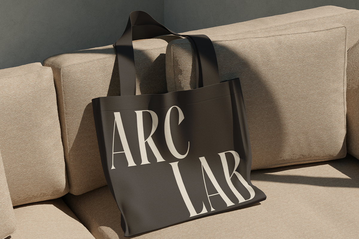 Black tote bag with serif branding mockup draped over beige linen couch