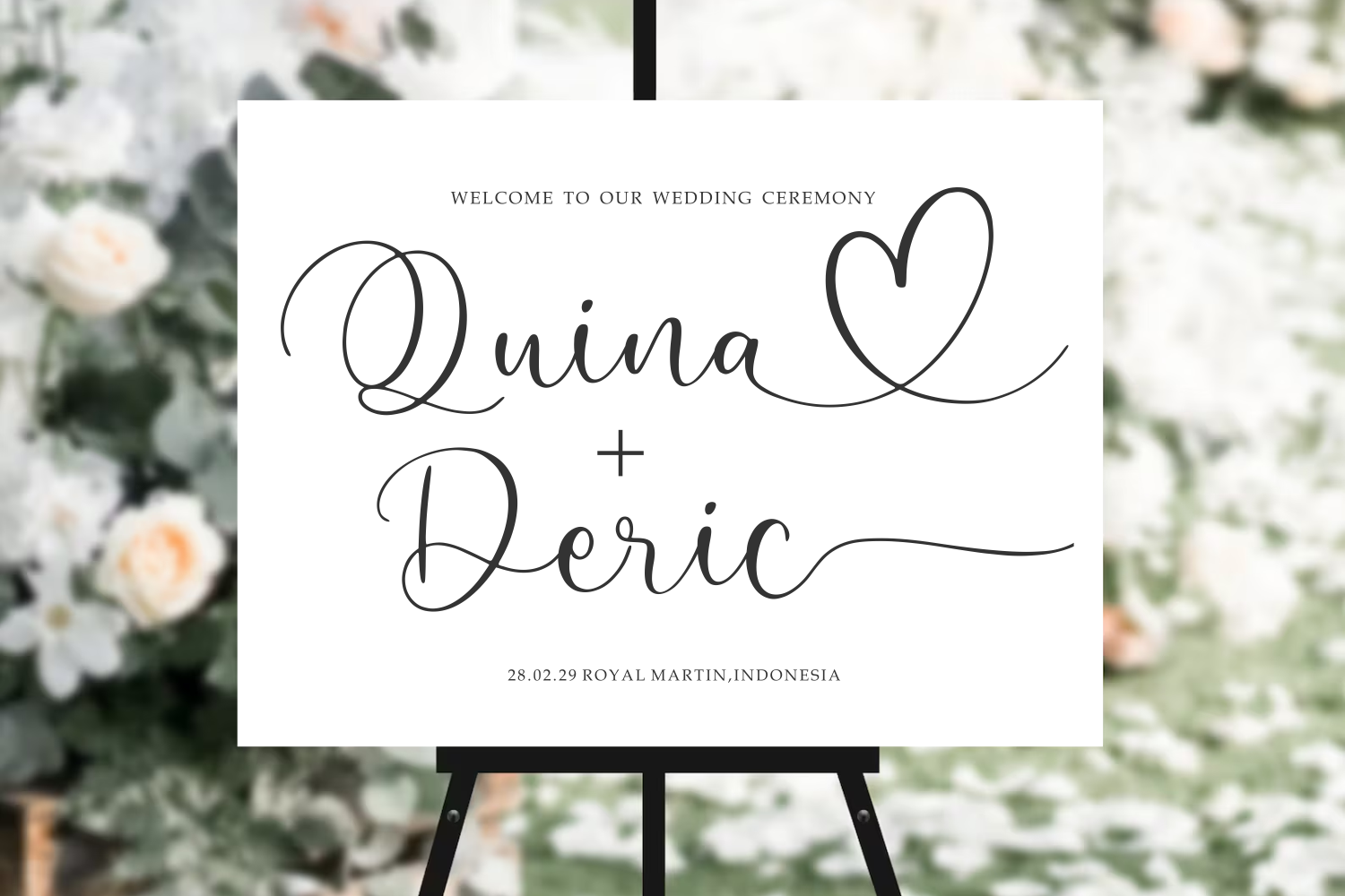 Wedding ceremony welcome sign with cursive names, heart illustration, date, location displayed on easel with floral backdrop