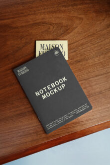 Dark notebook with branding laid on wood surface alongside cream business card mockup