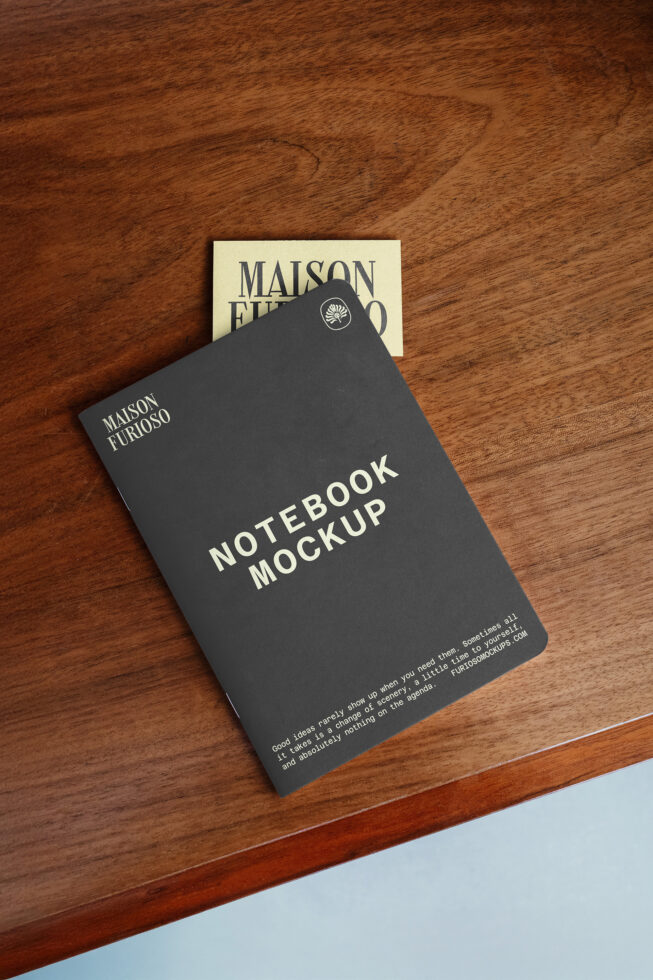 Dark notebook with branding laid on wood surface alongside cream business card mockup