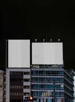 Blank billboards lit up at night mounted on urban buildings with dark sky