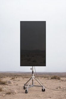 Mobile billboard mockup showing blank dark screen on tripod stand in desert landscape