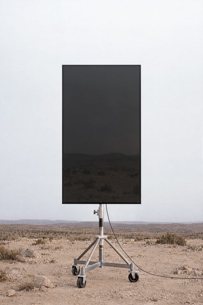 Mobile billboard mockup showing blank dark screen on tripod stand in desert landscape