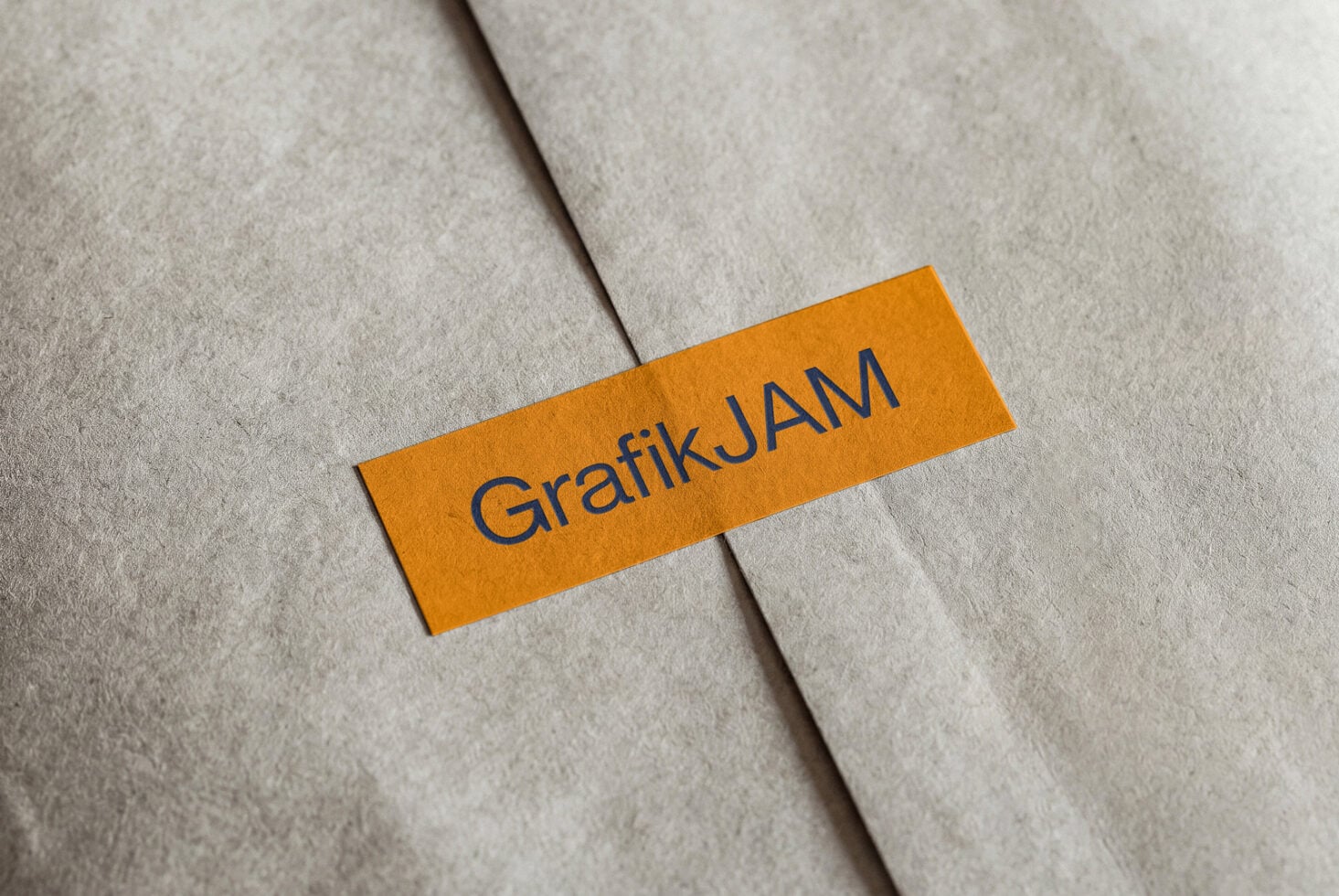 Bright orange label with GrafikJAM text on folded cream paper mockup