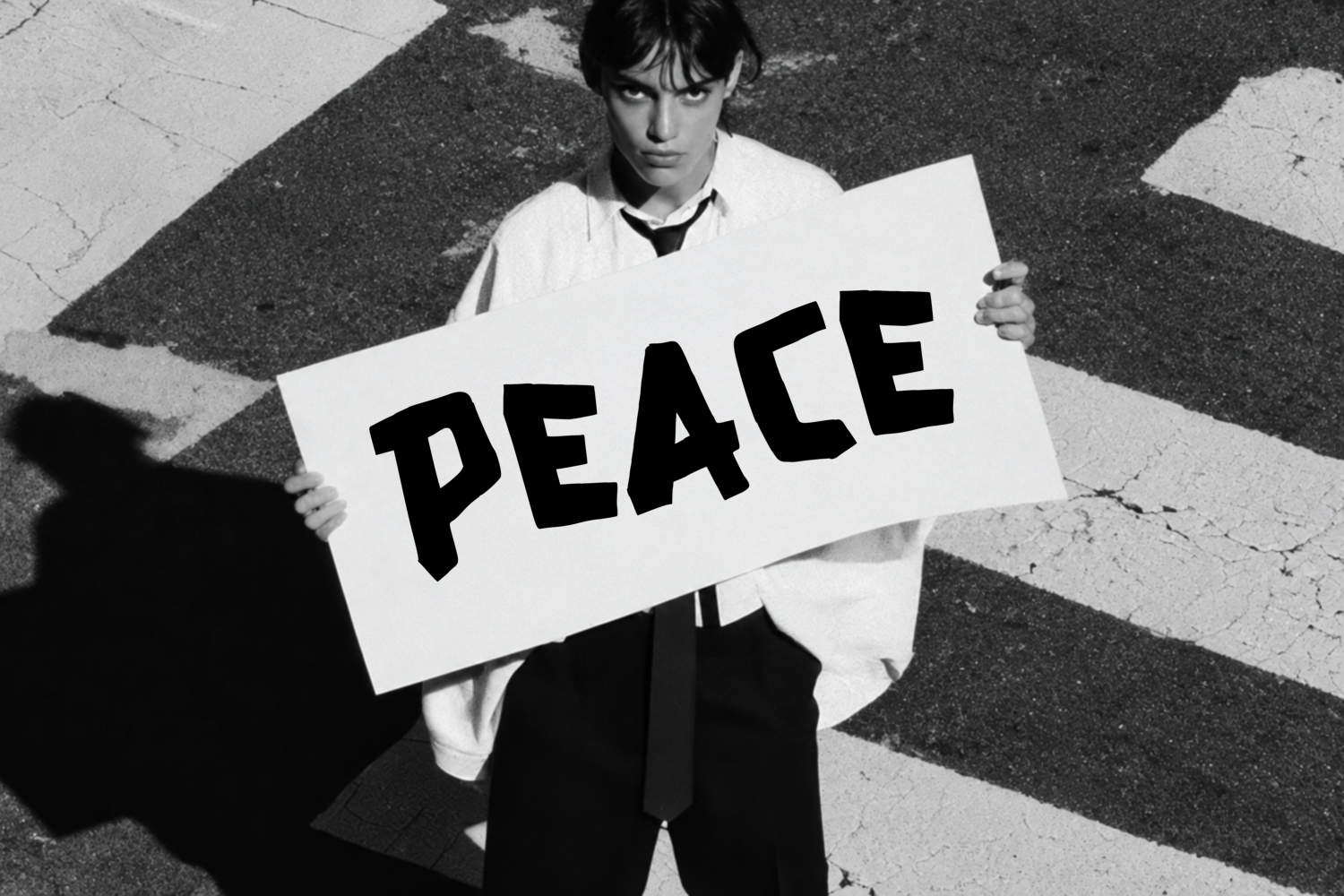 Black and white overhead shot of person holding peace sign poster on pavement