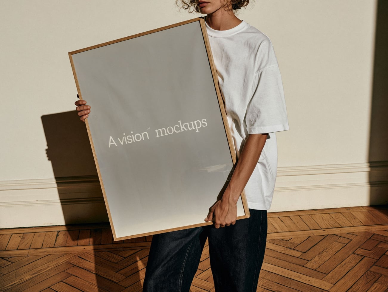 Person holding wooden framed poster mockup in bright studio with parquet flooring