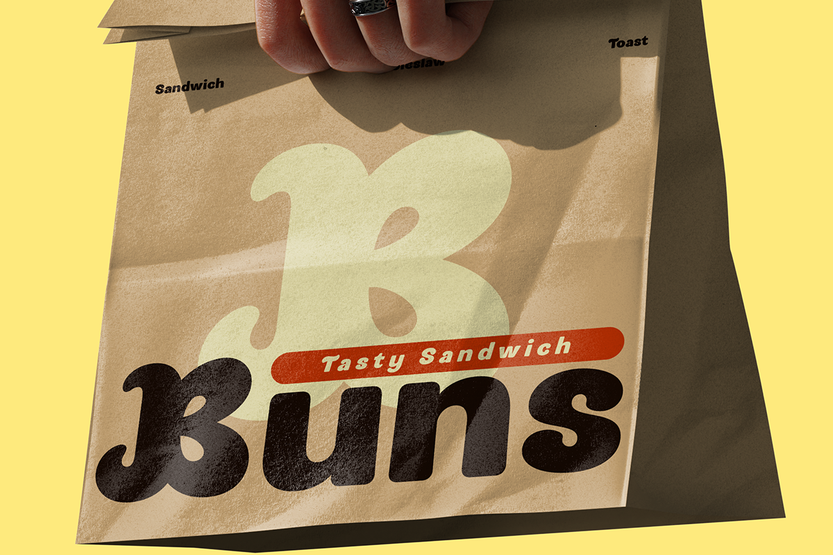 Hand holding kraft paper bag labeled "3 Buns Tasty Sandwich" with sandwich, toast text visible on bright yellow background