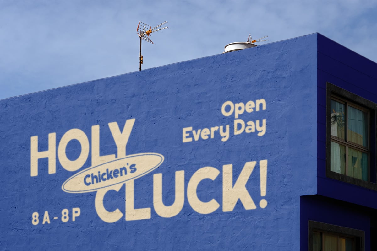 Bright blue building facade with vintage cream lettering for Holy Chicken's Cluck restaurant sign