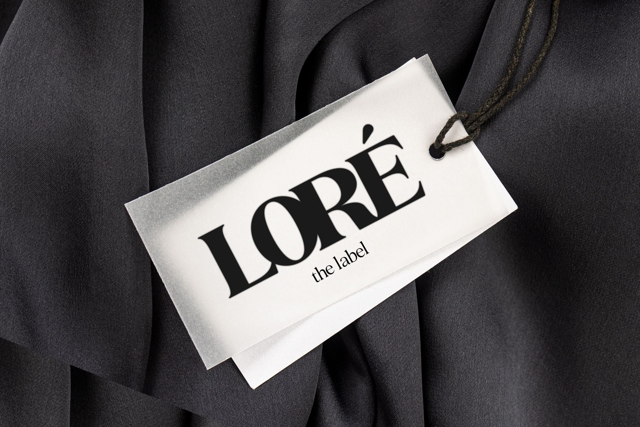 Minimalist clothing tag mockup with serif branding on cream cardstock draped over charcoal fabric