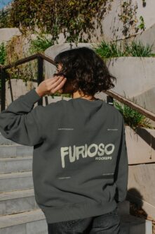 Person wearing charcoal sweatshirt with Furioso Mockups back print on urban deck with climbing vines