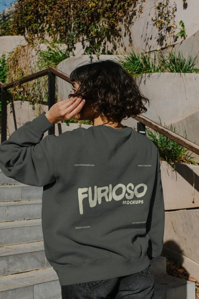 Person wearing charcoal sweatshirt with Furioso Mockups back print on urban deck with climbing vines