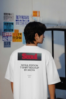Person wearing white tee with Seoul graphic back print standing in front of Korean signage