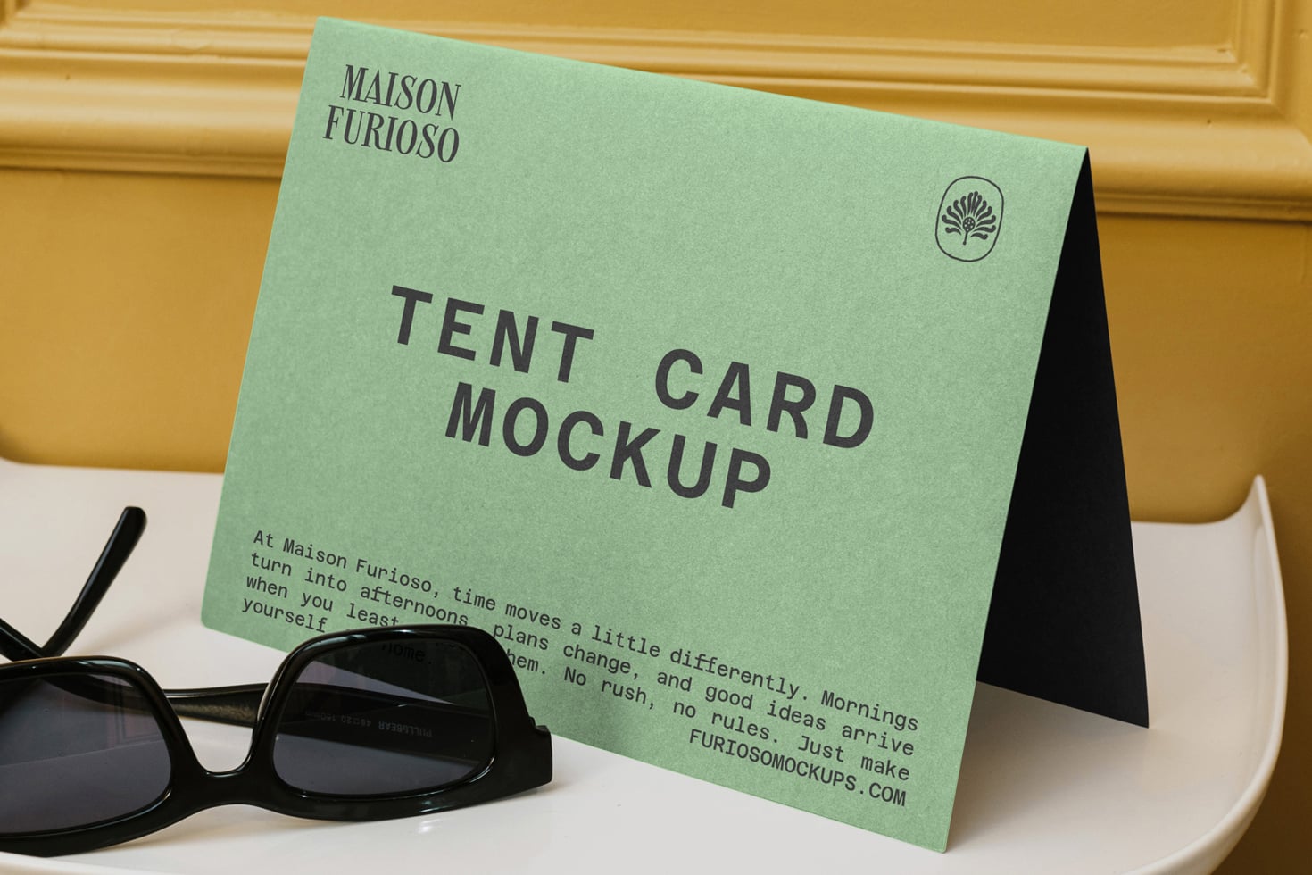 Mint green tent card mockup on white surface with sunglasses, gold wall behind