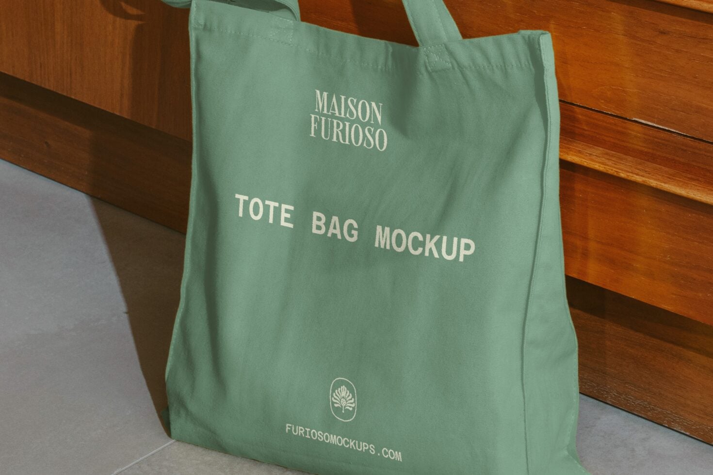 Sage green tote bag with cream text showing brand name, logo, on wooden floor