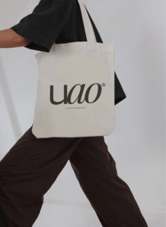 Hand holding natural canvas tote bag with uao logo printed in charcoal gray