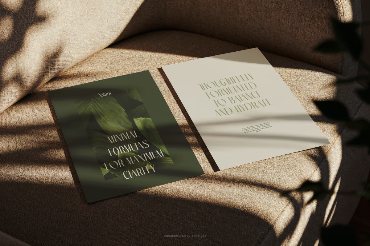 Two open brochures on brown linen with natural sunlight casting shadows, green botanical cover with cream interior pages