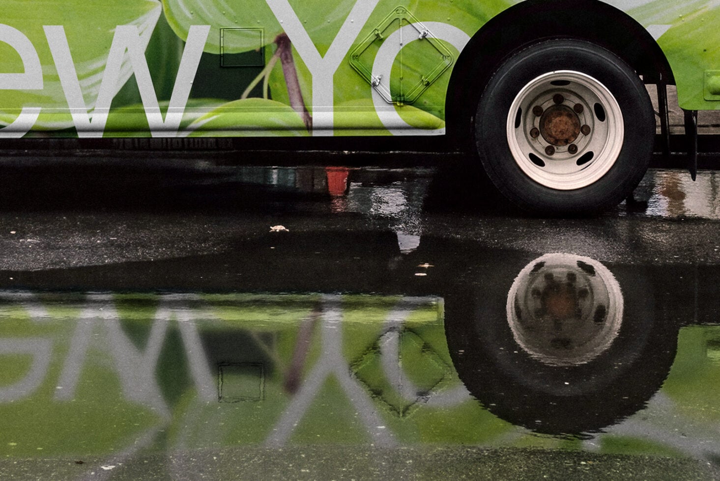 Bright lime green bus with white lettering parked in wet street, wheel reflection visible