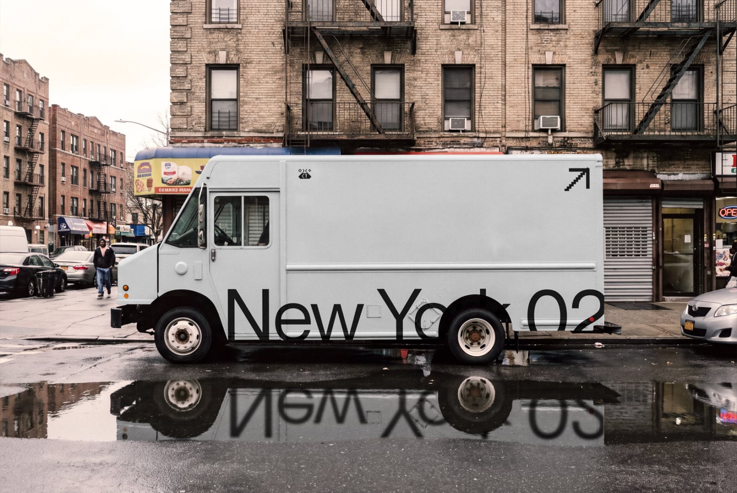 White delivery truck with "New York" text parked on wet street with brick buildings